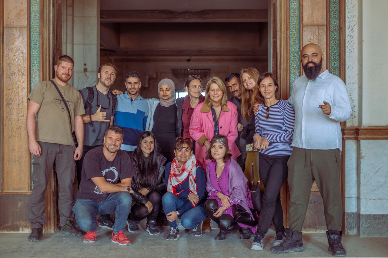 A diverse group of adults posing happily inside a historical building in Baghdad, Iraq.