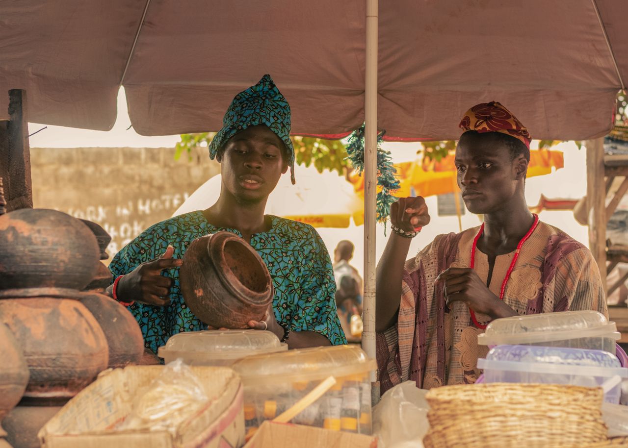 Two men in traditional attire selling pottery at an African market.
