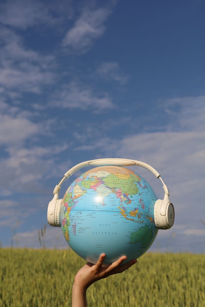 A globe wearing headphones in a field against a clear blue sky.